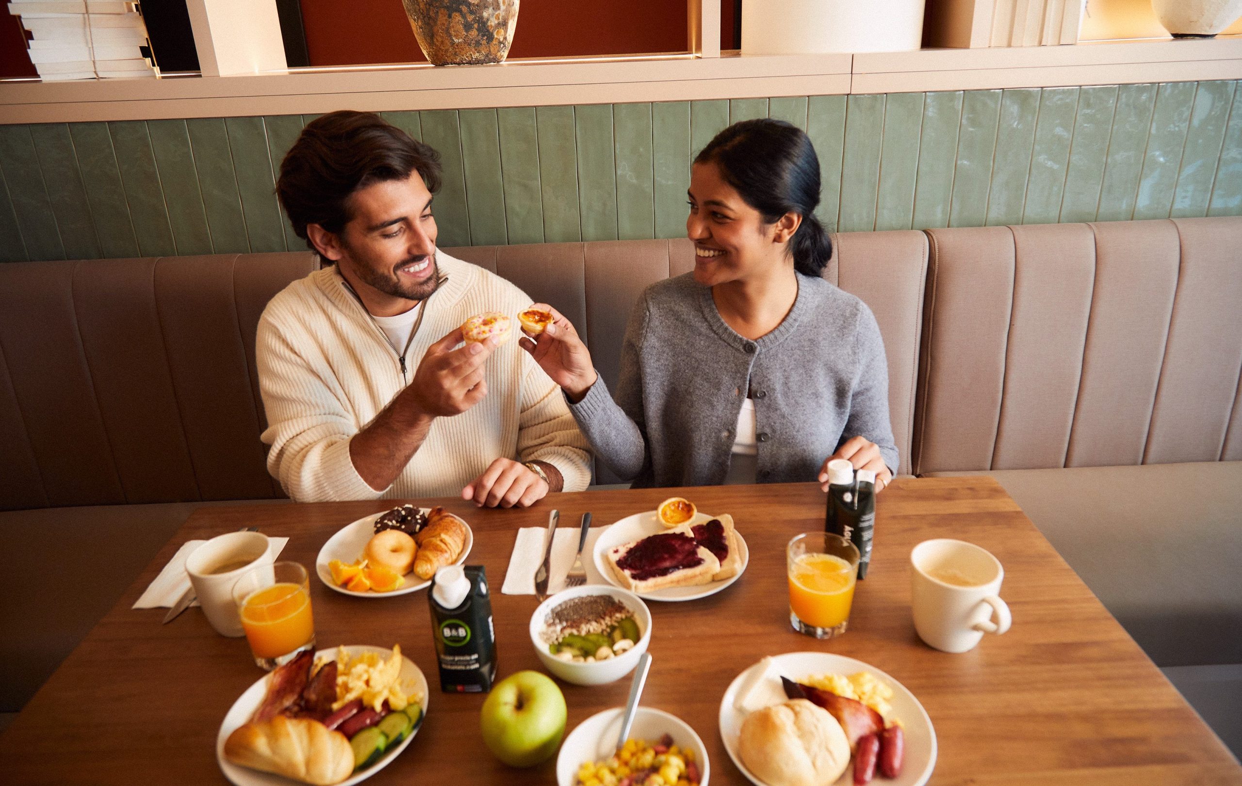 Couple enjoying the B&B HOTELS breakfast buffet with fresh pastries, fruit and orange juice