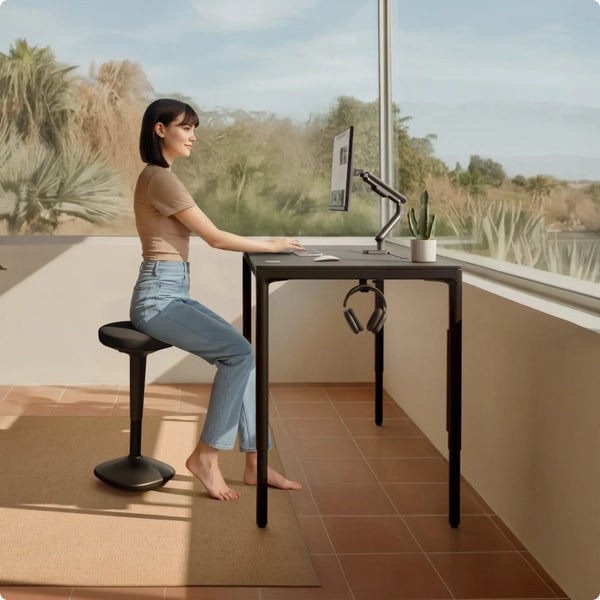 Person perched on a Desktronic balance stool at a standing desk