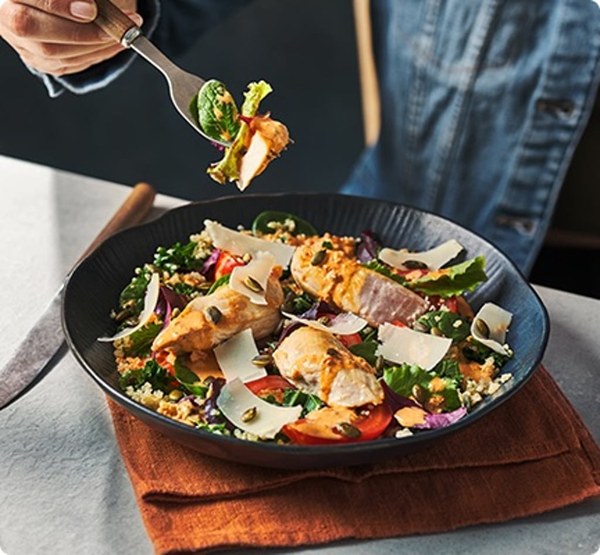 Bowl of salad with grilled chicken being eaten with a fork