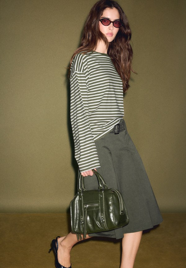 Model wearing a striped Stradivarius jumper with a khaki midi skirt and a dark green bag
