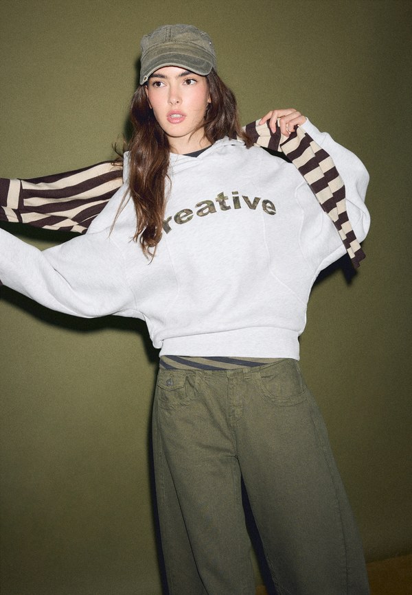Model in a Stradivarius college-style sweatshirt with wide striped sleeves, khaki trousers and a cap