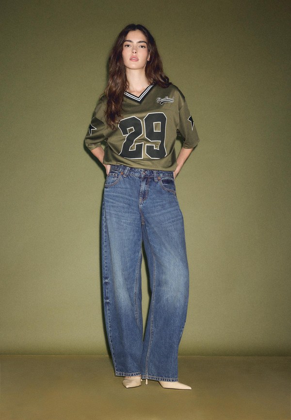 Model in a khaki sporty top and loose medium-blue jeans from Stradivarius