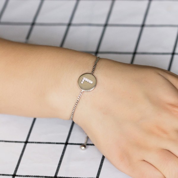 Wrist wearing a slim silver slider bracelet with a round disc initial charm