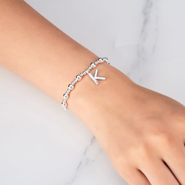 Wrist wearing a silver beaded stretch bracelet with a letter K charm