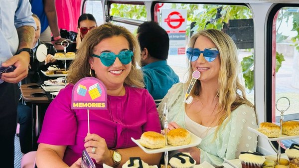 Two guests wearing sunglasses and holding party props on the ABBA-inspired afternoon tea bus