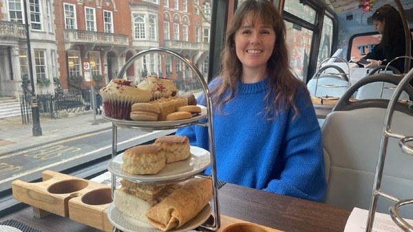 A guest seated at a table beside a window with sandwiches and scones on a tiered stand