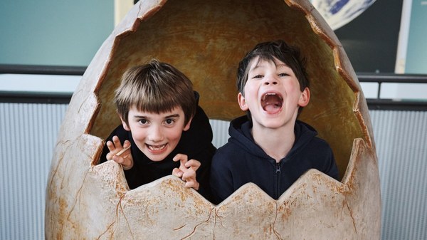 Two children peeking out of a giant dinosaur egg at the Life Science Centre