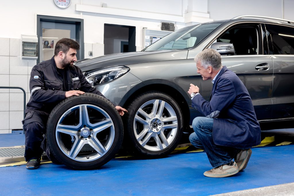 Winter Tyres in Austria: How to Choose, Buy and Fit the Right Set Online Tyre specialist advising a driver next to an SUV wheel